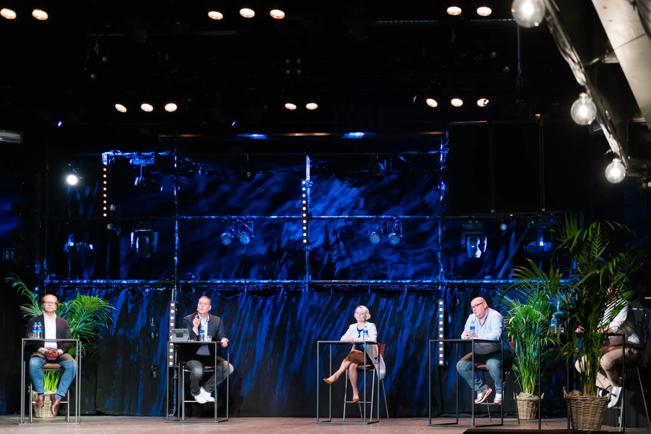 Eventfoto van een paneldiscussie op een podium in blauw licht