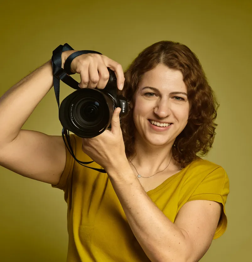 Joanna Vunderink in een geel shirt, lachend met haar camera